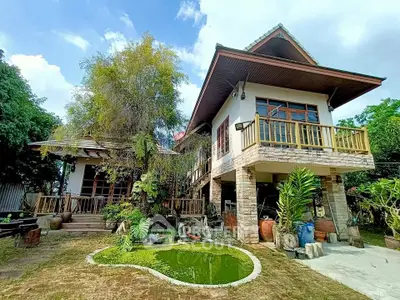 Charming two-story house with lush garden and small pond, featuring rustic stone accents and wooden balcony.