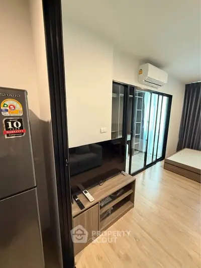 Modern apartment interior with sleek design, featuring a compact living area and bedroom with sliding glass doors.