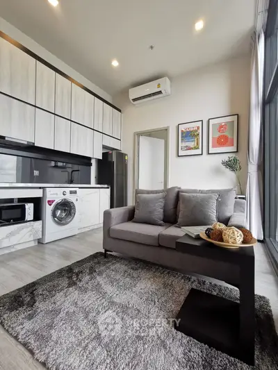 Modern living room with sleek kitchen, featuring washing machine and stylish decor.