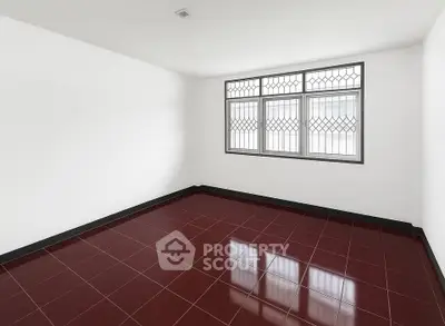 Spacious empty room with red tiled floor and large window, perfect for customization.
