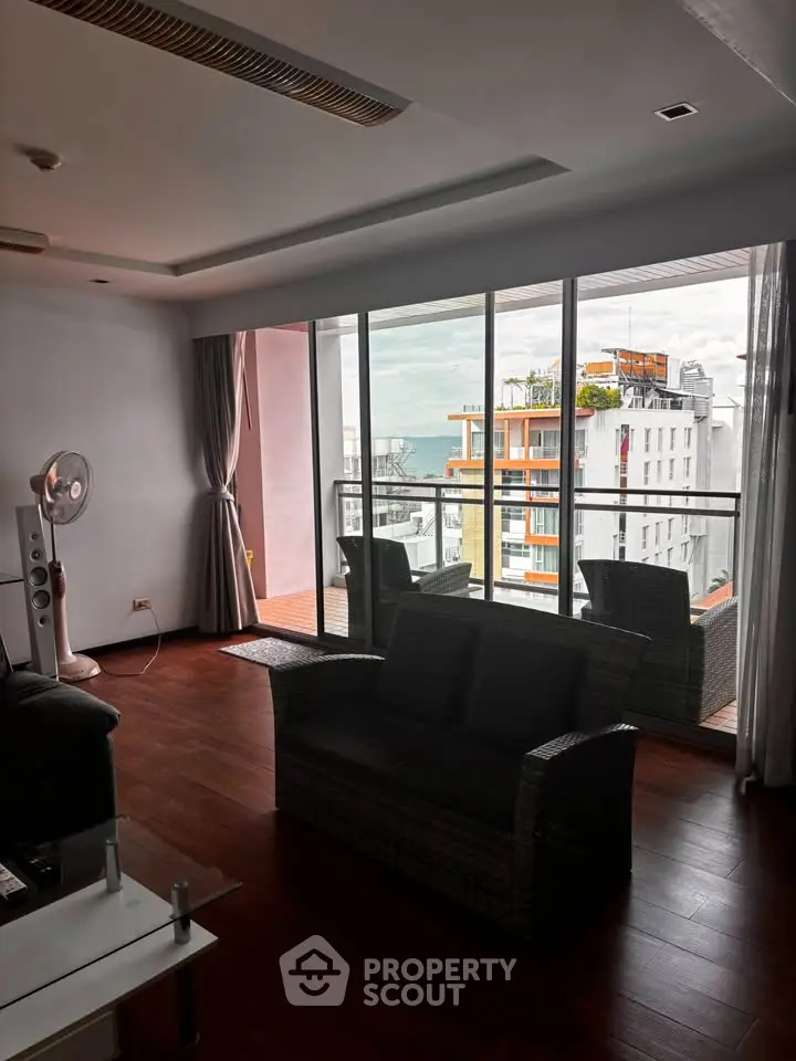 Spacious living room with large windows and balcony offering stunning city views.