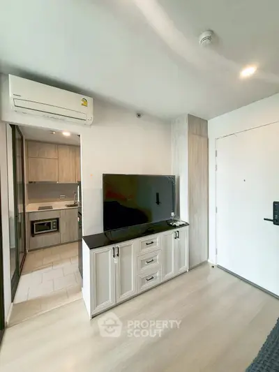 Modern apartment interior with sleek kitchen and stylish living area featuring a large TV and air conditioning.