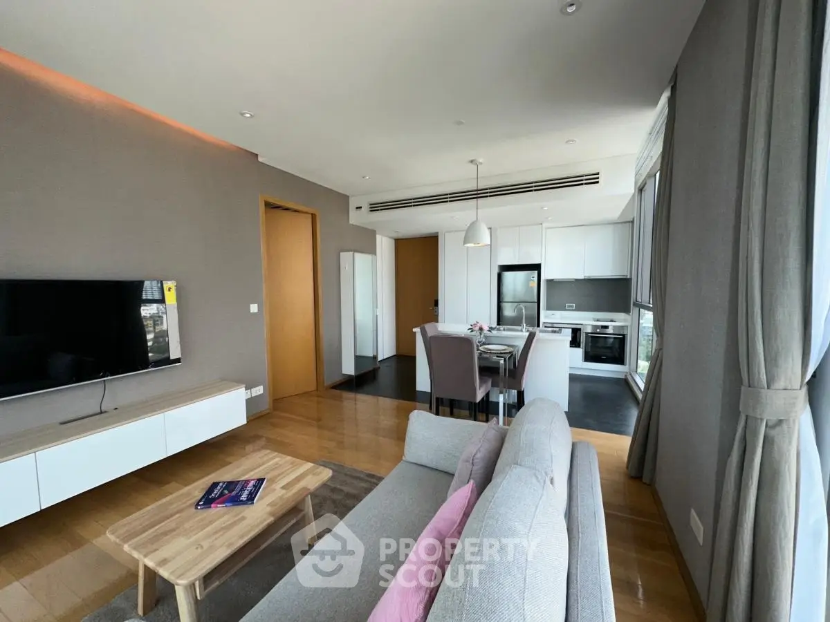 Modern open-plan living room with kitchen, featuring sleek design and large windows for natural light.