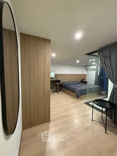 Modern bedroom with wooden flooring and glass partition, featuring a cozy bed and stylish decor.