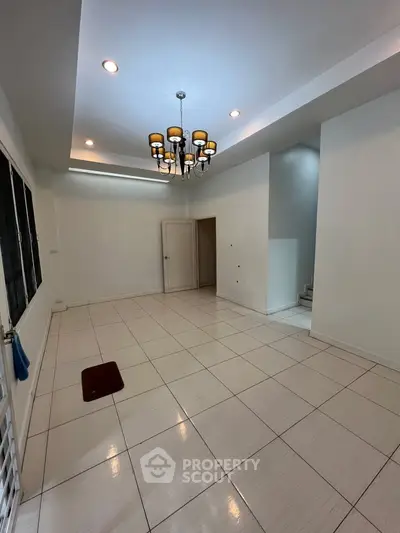Spacious empty room with elegant chandelier and tiled flooring, perfect for customization.
