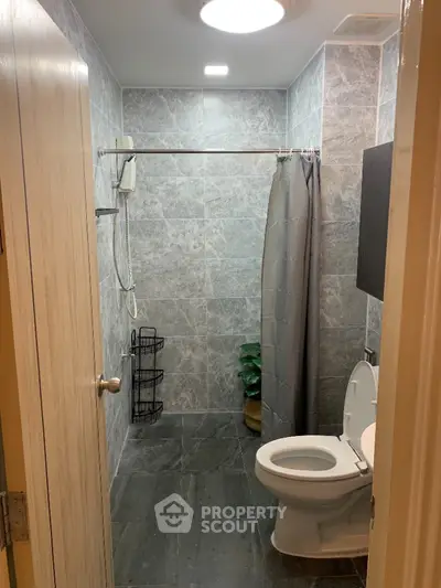 Compact modern bathroom with grey tiled walls and flooring, featuring a shower area with curtain, toilet, and essential amenities for a functional urban living space.