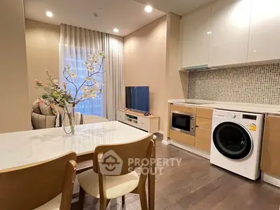 Modern living room with open kitchen, featuring washing machine and microwave, elegant decor and dining area.