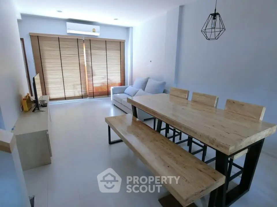 Modern living room with natural wood dining set and cozy sofa, featuring stylish lighting and large windows.