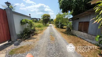 Charming rural pathway with lush greenery and rustic buildings, perfect for serene living.