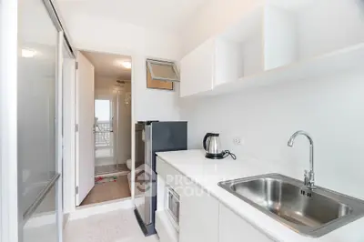 Modern kitchen with sleek white cabinetry and stainless steel sink, adjacent to a bathroom with glass shower.