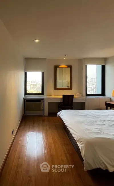 Spacious bedroom with wooden flooring and city view, featuring a cozy bed and a work desk.