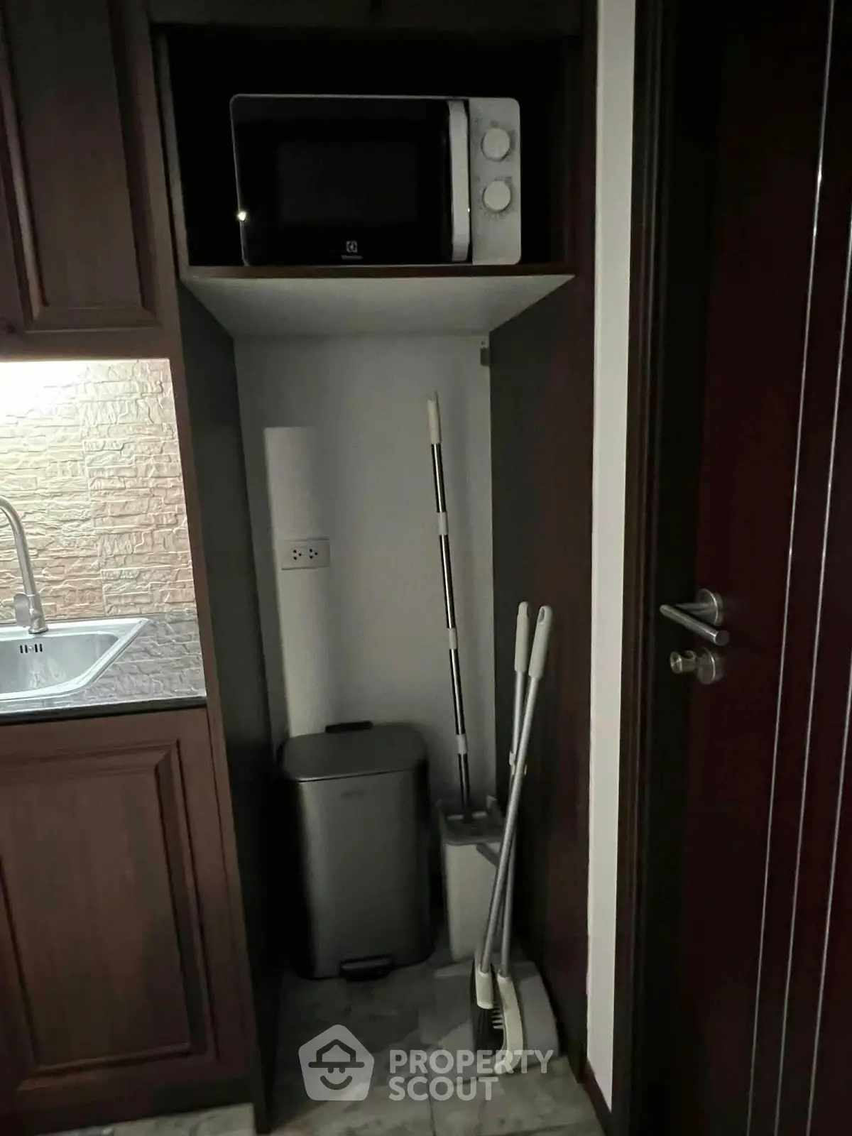 Compact kitchen corner with microwave and cleaning tools in modern apartment.