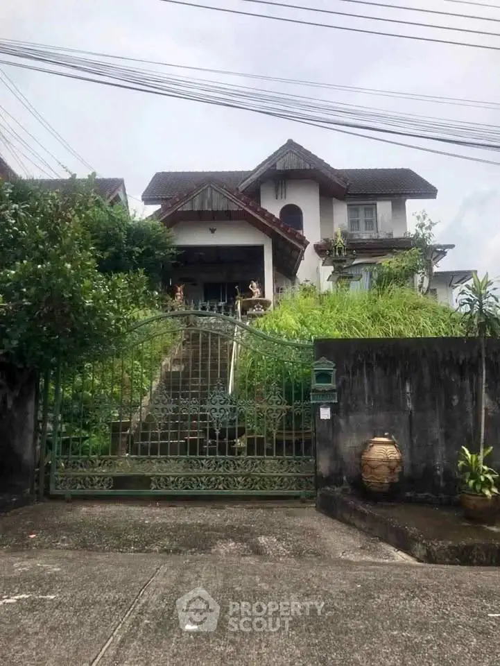 Charming two-story house with lush garden and ornate gate, perfect for family living.
