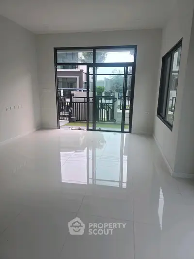Spacious modern living room with large windows and glossy white tiles.