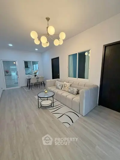 Modern living room with elegant chandelier and cozy seating area, open layout leading to dining space.
