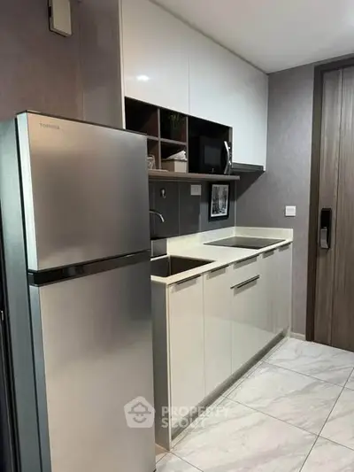 Modern kitchen with sleek cabinetry and stainless steel fridge in a compact layout.