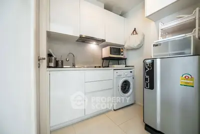 Modern compact kitchen with washing machine and microwave in sleek white cabinetry.