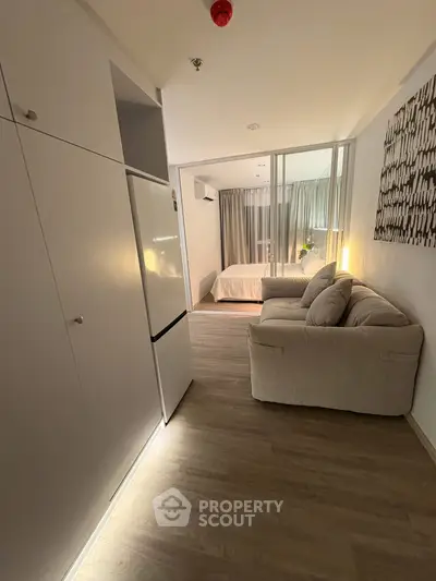 Modern studio apartment with cozy living area and bedroom, featuring sleek white cabinetry and warm lighting.