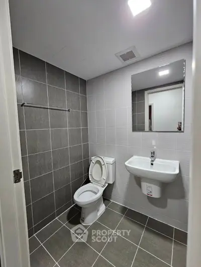 Modern bathroom with sleek gray tiles and white fixtures, featuring a wall-mounted sink and toilet.