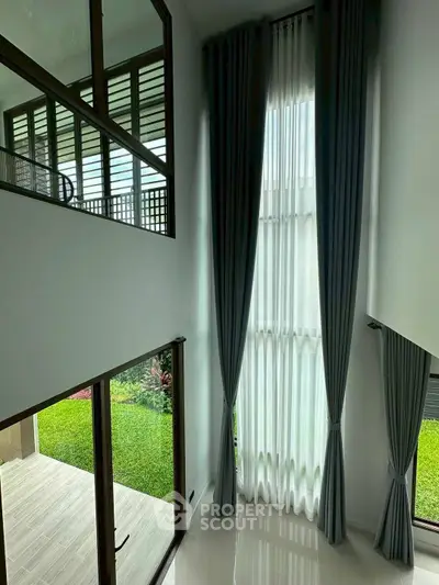 Spacious modern living room with high ceilings and large windows overlooking a lush garden.