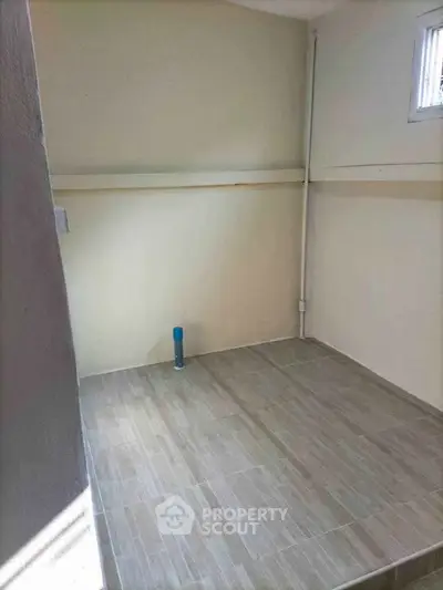 Minimalist empty room with tiled flooring and small window, ideal for storage or utility use.