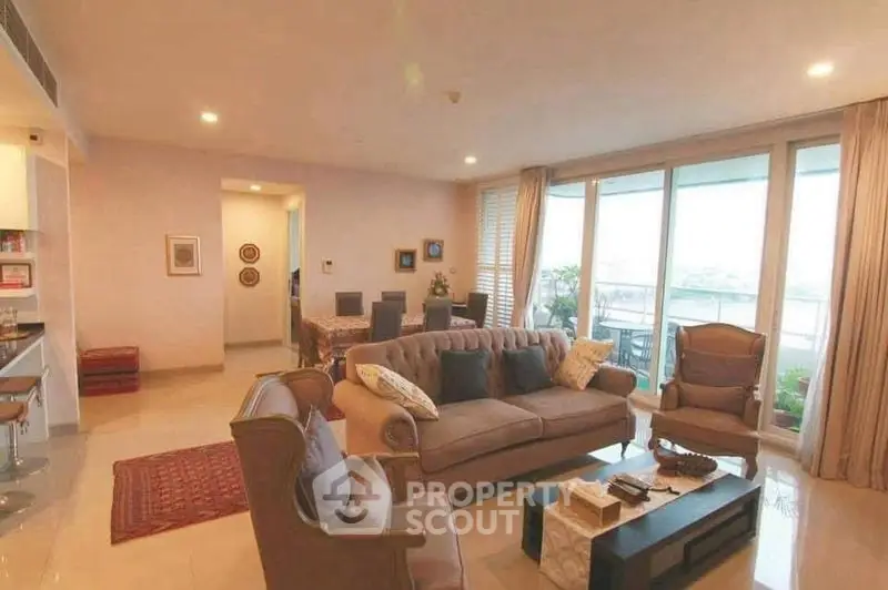 Spacious living room with elegant furniture and large windows leading to a balcony with a view.