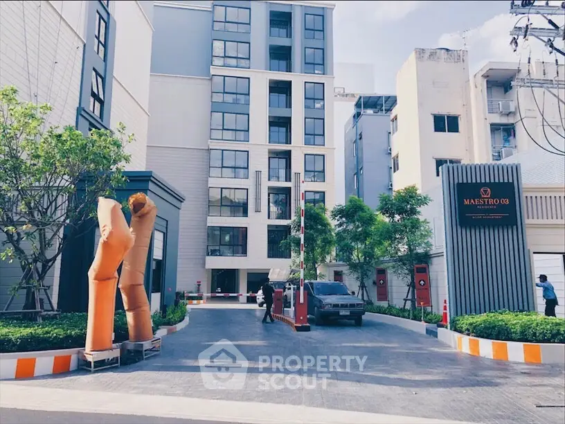 Modern apartment building entrance with security gate and vibrant landscaping.