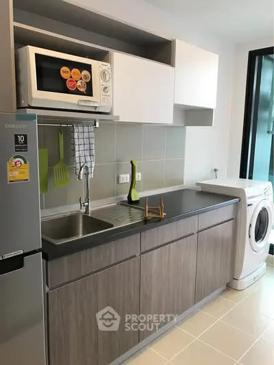 Modern kitchen with sleek cabinets, microwave, fridge, and washing machine in a compact layout.