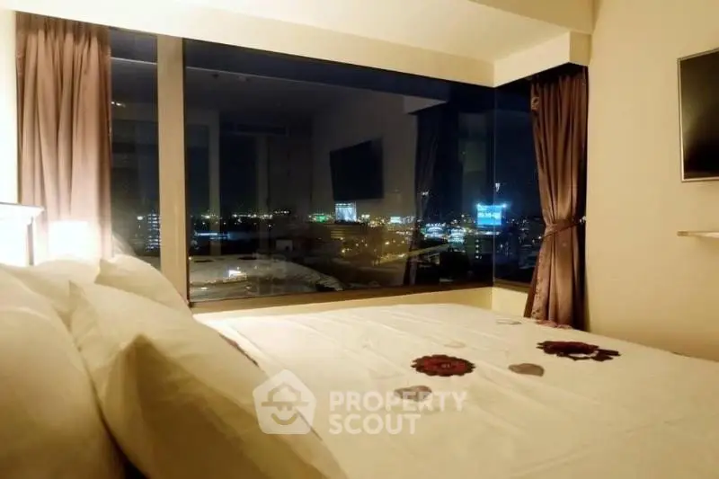 Luxurious bedroom with stunning city view through large windows at night.