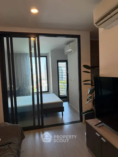 Modern apartment interior with sliding glass doors and city view, featuring a cozy bedroom and living area.