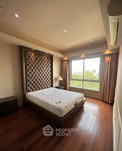 Luxurious bedroom with elegant wood flooring and large window offering a serene view, perfect for relaxation.