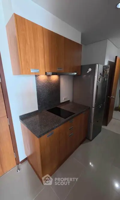 Modern kitchen with sleek wooden cabinets and stainless steel fridge in a compact layout.