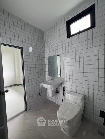 Modern bathroom with tiled walls and window, featuring a toilet and sink in a new construction.