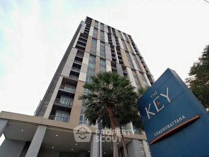 Modern high-rise building with sleek design and lush palm trees at The Key Chaengwattana.