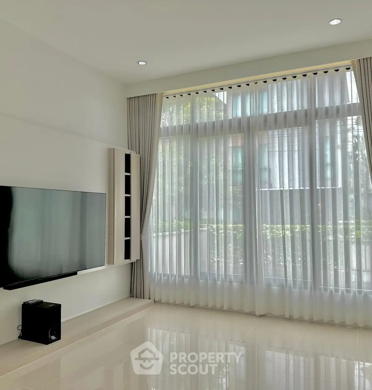Spacious living room with large windows and modern TV setup, offering abundant natural light.