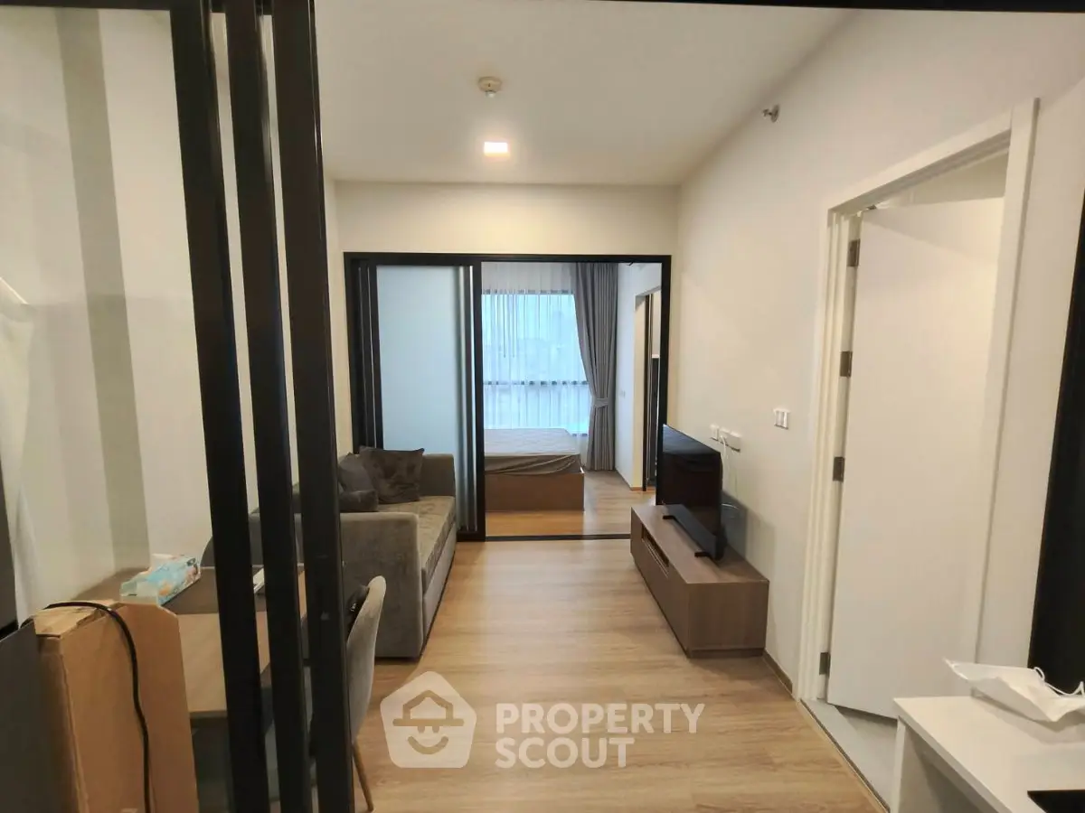 Modern apartment interior with open living room and bedroom view, featuring sleek furniture and wooden flooring.