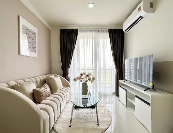 Modern living room with elegant sofa, glass coffee table, and large TV, featuring natural light from floor-to-ceiling windows.