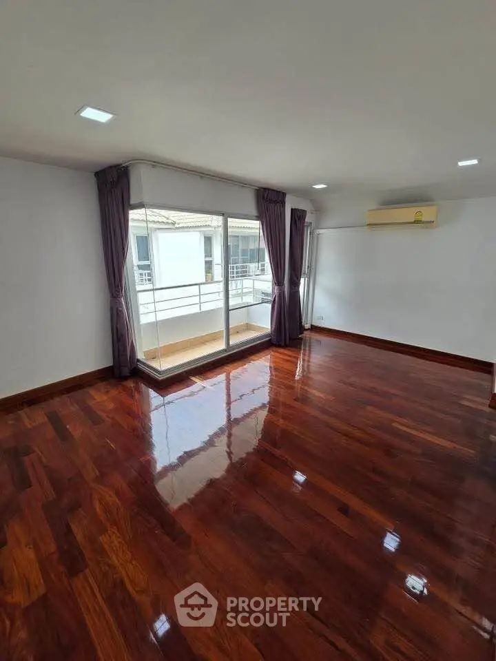 Spacious corner unit with polished hardwood floors and large windows leading to a balcony.