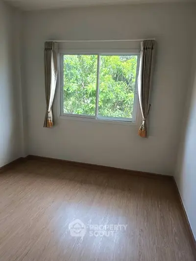 Bright empty room with large window and wooden flooring, perfect for customization.