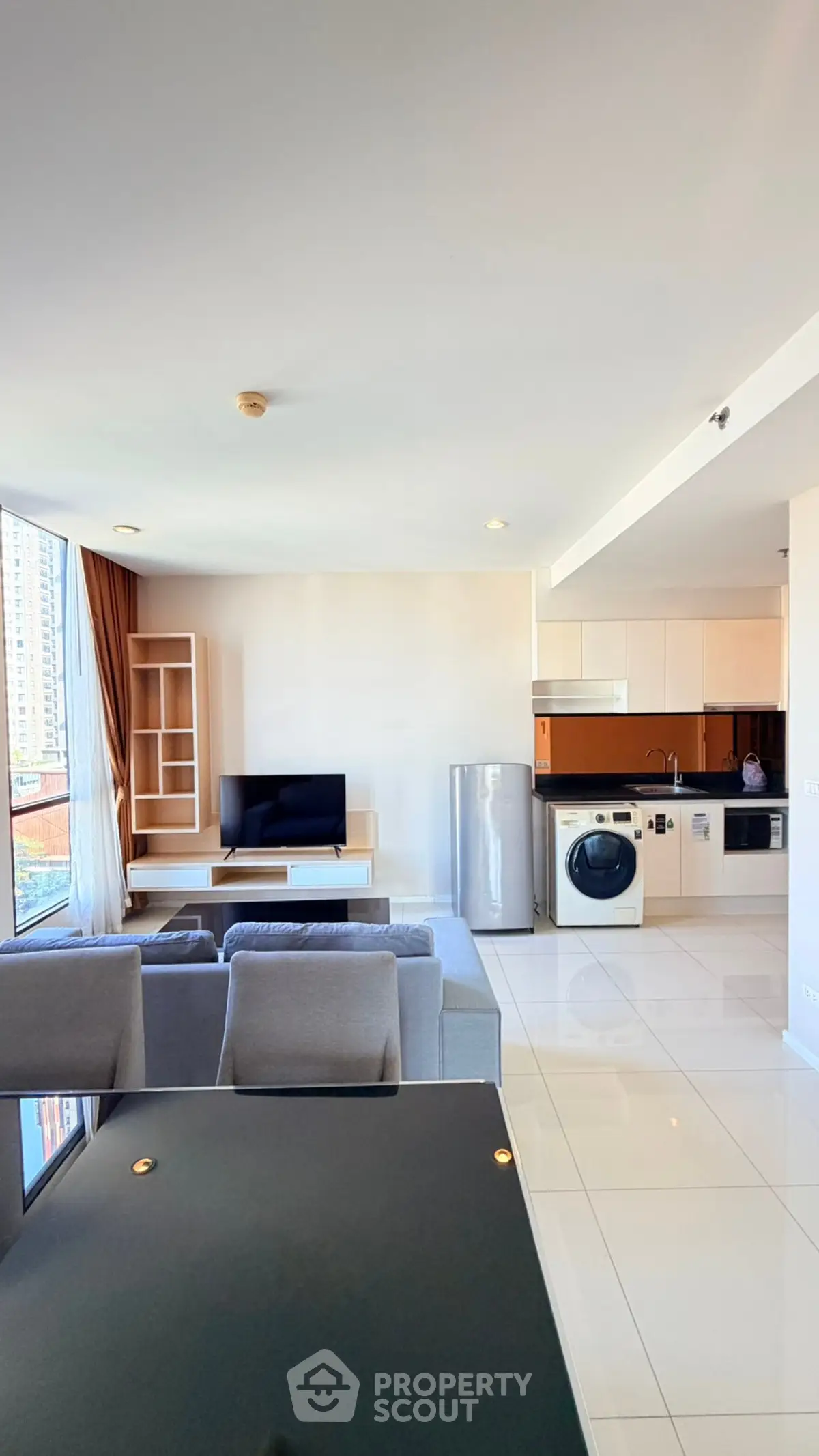 Modern open-plan living room with kitchen, featuring sleek appliances and large windows.