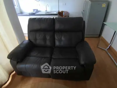 Cozy living room with black leather sofa and modern kitchen in background