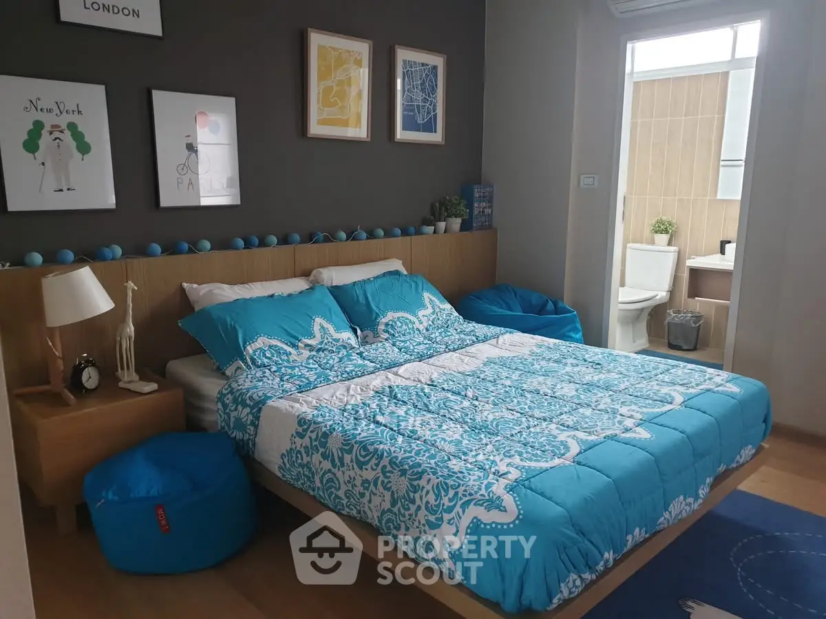 Modern bedroom with stylish decor and ensuite bathroom, featuring vibrant blue bedding and wall art.