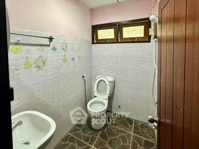 Cozy bathroom with tiled walls and floor, featuring a toilet, sink, and shower area.