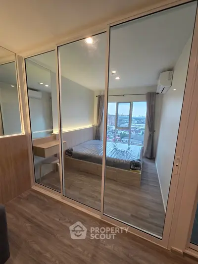 Modern bedroom with mirrored closet and city view, featuring sleek design and natural light.