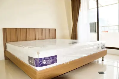 Spacious bedroom with modern wooden bed frame and large windows offering natural light.
