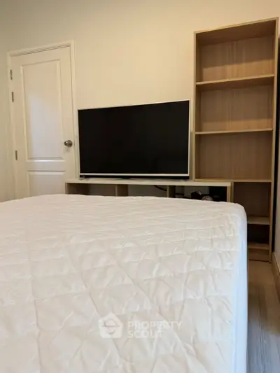 Cozy bedroom with modern TV setup and wooden shelving, perfect for relaxation.