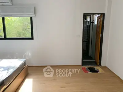 Spacious bedroom with wooden flooring and en-suite bathroom, featuring a large window with natural light.