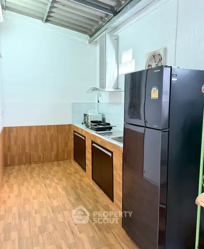 Modern kitchen with sleek black fridge and wooden flooring, featuring a gas stove and ample storage.