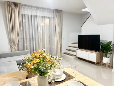 Modern living room with stylish decor and staircase, featuring a cozy sofa and elegant dining setup.