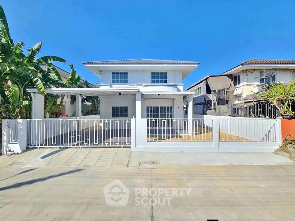 Modern two-story house with white facade and gated driveway in sunny neighborhood.